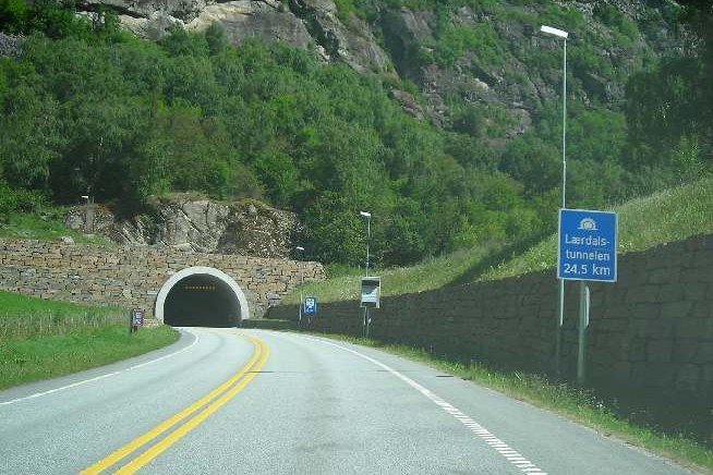 The entrance to the Lærdal Tunnel in Norway, a portal set into a rock face with the approach road and low retaining walls.
